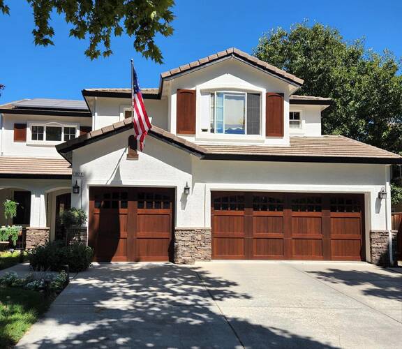 home with bright white paint on stucco, rock facade accents, and redwood garage doors